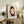 May include: Framed art print featuring a stylized illustration of a young girl with brown bob haircut and green eyes, wearing a dark shirt against a light background. The poster displays "YOSHITOMO NARA" text at bottom. Shown in thin wooden frame, positioned on rustic wooden sideboard alongside fern plant, ceramic vase, and books in neutral-toned living room setting.