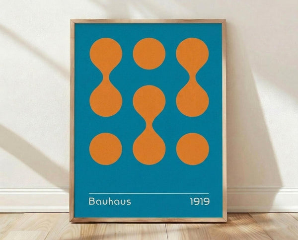 May include: Framed geometric art print with turquoise blue background and orange circular shapes arranged in a 3x3 grid pattern. Two circles on left and right sides connect to form hourglass or figure-8 shapes, while center column shows three separate circles. White text at bottom reads "Bauhaus 1919". Natural wood frame sits on light wooden floor against white wall with soft shadow cast behind it.