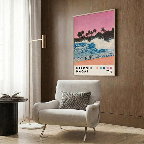 May include: Framed poster showing tropical beach scene with pink sunset sky, palm trees, blue ocean waves, and two small figures on sandy shore. Displayed on wood-paneled wall above cream upholstered armchair with geometric patterned pillow. Modern brass floor lamp and dark round side table with open book complete the minimalist living room setting with light wood flooring and white curtains.