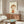 May include: Framed artwork featuring a stylized child with brown hair wearing an orange striped shirt, displayed above a wooden sideboard in a modern living room with white curved chair, glass coffee table, and warm natural lighting creating shadows across the scene.