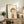 May include: Framed art print featuring a stylized illustration of a young child with orange-brown hair and closed eyes, wearing an orange-red shirt, displayed on a rustic wooden sideboard alongside decorative pottery, books, and a fern plant in a cozy living room setting with neutral tones and soft lighting.