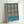 A geometric poster with orange circles and connecting shapes arranged in a 3x3 grid pattern on a bright blue background. The text "Bauhaus 1919" appears in white at the bottom. The artwork is displayed in a thin light wood frame and leaning against a white wall, casting a soft shadow.