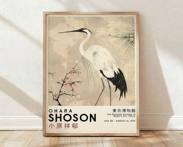 May include: Framed poster print featuring a white crane with black wing tips and long curved neck, standing among delicate branches with small red berries and pine needles, rendered in soft beige and cream tones in traditional Japanese art style. Text reads "OHARA SHOSON" with Japanese characters and museum exhibition details from 1972. Light wood frame sits against white wall on wooden floor with natural lighting.