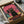 May include: Framed colorful cat illustration artwork being unboxed from shipping materials. Black cat with yellow collar sits prominently on rooftop with pink and coral background. Multiple outline cats with sunglasses fill the scene. Vibrant retro color palette includes coral pink, orange, yellow and teal. Print appears mounted in dark frame, surrounded by protective packaging materials and cardboard box.