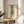 May include: Framed fashion illustration print on wooden side table next to beige upholstered chair and plant. Artwork shows legs in black and white striped pants with red high heel shoes against cream background in light wood frame. Soft natural lighting creates shadows across neutral-toned room setting.