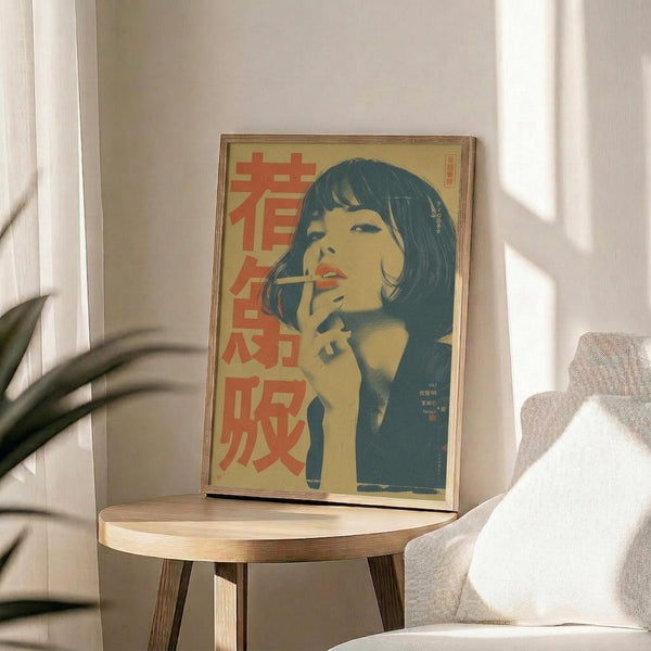 May include: Framed vintage-style poster featuring a woman with dark bob haircut smoking, rendered in yellow and teal tones with red Japanese characters, displayed on a round wooden side table next to a beige upholstered chair with white pillow, green plant leaves visible in corner, natural lighting casting shadows on white wall