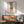 May include: Framed poster showing legs in black and white striped pants with red heels, displayed above a wooden sideboard with table lamp in modern living room setting with mint green armchair and natural sunlight creating shadows on white wall.