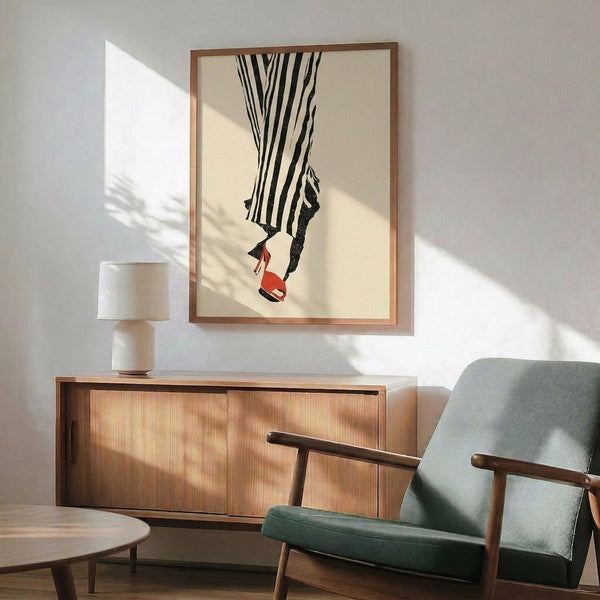 May include: Framed poster showing legs in black and white striped pants with red heels, displayed above a wooden sideboard with table lamp in modern living room setting with mint green armchair and natural sunlight creating shadows on white wall.