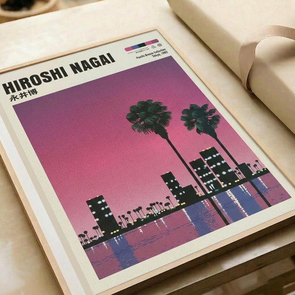 A framed poster print featuring a vibrant pink sunset sky over a silhouetted waterfront cityscape with two prominent palm trees in the foreground. The minimalist artwork shows dark building silhouettes reflected in purple-blue water below. The print is displayed in a light wooden frame against white paper or packaging material with a beige ribbon visible in the corner.