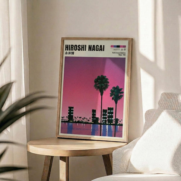 May include: Framed poster with pink-purple gradient sky, silhouetted palm trees and city skyline reflected in water, displayed on round wooden side table next to beige upholstered chair. Natural wood frame complements the table's light finish. Soft window lighting creates shadows on white wall behind, with partial view of plant leaves in corner.