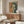 May include: Vintage Japanese movie poster featuring woman with dark bob haircut smoking cigarette, rendered in yellow and teal tones with red text characters. Poster displayed above mid-century walnut credenza in modern living room with white upholstered chair, glass coffee table, and copper floor lamp.