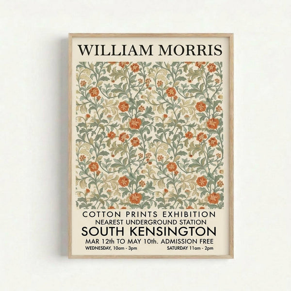 A framed vintage-style exhibition poster featuring William Morris floral pattern in sage green, coral orange, and cream colors. The decorative botanical design shows flowing vines, leaves, and flowers in an Arts and Crafts style. Black text advertises a cotton prints exhibition in South Kensington with dates and admission details. The poster is displayed in a light wood frame against a white wall.