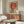 May include: Vintage-style poster featuring woman in dark blue cheongsam dress sitting on wooden stool against large red circle background with Asian characters, displayed in warm wood frame above mid-century walnut credenza in minimalist room with white sculptural chair, table lamp, and oval glass coffee table