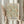 May include: Hands holding a framed poster featuring William Morris floral pattern in sage green and coral orange against cream background. Exhibition poster design with Cotton Prints Exhibition and South Kensington text. Light wood frame, neutral room setting with dried wheat stems and flowing curtains visible.