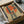 May include: Framed vintage-style poster artwork showing a woman in dark cheongsam dress sitting on wooden stool against large red circle backdrop, with blue Japanese characters in upper right corner, displayed in black frame inside cardboard shipping box with white tissue paper padding