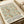 May include: Vintage-style exhibition poster featuring William Morris floral pattern in sage green and terracotta orange on cream background. The decorative botanical design shows intertwining vines and blooms. Text indicates cotton prints exhibition at South Kensington with dates and admission details. Poster appears unframed on white paper, photographed alongside rolled paper tubes on neutral surface.