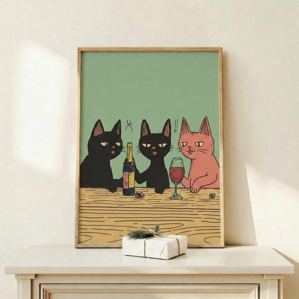 May include: Framed poster print showing three cartoon cats sitting at wooden table with wine bottle and glass. Two black cats and one pink/coral cat with sleepy expressions against sage green background. Natural wood frame displayed on white shelf next to small wrapped gift with greenery sprig.