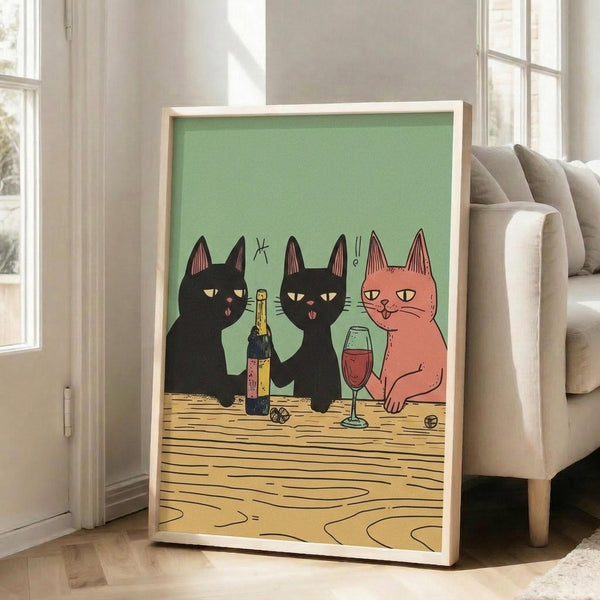 May include: Framed poster print leaning against white wall next to beige sofa in bright room with windows. Artwork shows three stylized cats sitting at wooden table - two black cats and one orange cat - sharing wine bottle and glass against sage green background. Light wooden frame, approximately 2-3 feet tall based on sofa scale.
