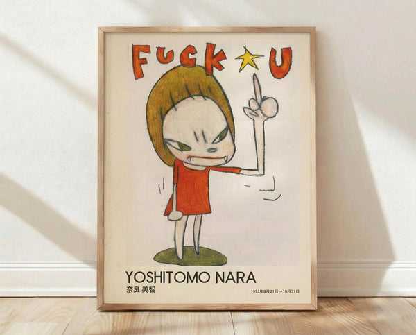 May include: Framed art print leaning against white wall on light wood floor. Artwork shows cartoon-style character with blonde bob haircut wearing red dress, making middle finger gesture. Text reads "F*ck U" in red letters at top and "YOSHITOMO NARA" with Japanese characters and date at bottom. Natural wood frame with cream matting, soft natural lighting creating diagonal shadows.
