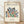May include: Framed art print featuring colorful cut-out style botanical shapes in blue, green, red, orange and black arranged in a bouquet pattern. Text reads "MATISSE" at top, "Hammer Museum University of California US" below, and "La gerbe Henri Matisse, 1953" at bottom. Light wood frame against cream textured wall with white baseboard, sitting on light wooden floor with natural shadows.
