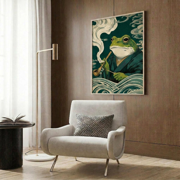 May include: Japanese-inspired artwork featuring a green frog in dark robes smoking a pipe, surrounded by swirling clouds and stylized waves in traditional ukiyo-e style with teal and cream colors. The poster is displayed in a light wood frame on wood paneled walls above a beige upholstered chair with geometric pillow, next to a brass floor lamp and black side table with open book.