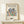 May include: Framed art print featuring Matisse's colorful cut-out style botanical design with blue, green, orange, and burgundy leaf shapes arranged in a circular pattern on cream background. Wooden frame sits on light wood shelf next to small wrapped gift with twine bow. Clean white wall backdrop creates minimalist home decor scene.