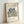 May include: Framed museum poster print featuring Matisse's colorful cut-out style botanical design with abstract leaf and coral shapes in blue, green, orange, red, and black on cream background. Light wood frame leaning against white wall, showing museum attribution text and artwork title below the vibrant organic pattern.