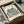 May include: Framed museum poster print featuring Henri Matisse's colorful botanical cut-out design with blue, red, green, orange and black leaf-like shapes arranged in circular pattern on cream background. Black frame sits in open cardboard shipping box with white tissue paper on wooden surface next to wrapped tube.