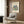 May include: Cream-colored poster with Henri Matisse's colorful botanical cutout design featuring blue, green, orange, and red leaf shapes arranged in a bouquet pattern. Shown framed in light wood frame hanging on wood-paneled wall above beige upholstered armchair with geometric throw pillow. Modern brass floor lamp and dark side table with open book visible in minimalist room setting.