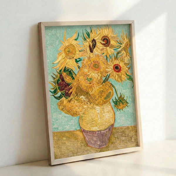 May include: Framed reproduction of Van Gogh's sunflowers painting leaning against white wall. Artwork shows vibrant yellow sunflowers in ceramic vase against turquoise background, displayed in light wood frame. Post-impressionist style with thick, textured brushstrokes visible throughout the composition.