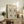 May include: Framed beige poster with black line drawings of faces and botanical elements in Matisse's minimalist style, displayed on rustic wooden sideboard alongside fern plant, ceramic vase, stacked books, and brown leather chair in neutral-toned living room setting.
