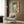 May include: Colorful Matisse-style painting hanging on wood-paneled wall above cream upholstered armchair with geometric pillow. Artwork shows vibrant green, pink, and orange interior scene with open window view. Modern reading nook with brass floor lamp and dark side table with open book.