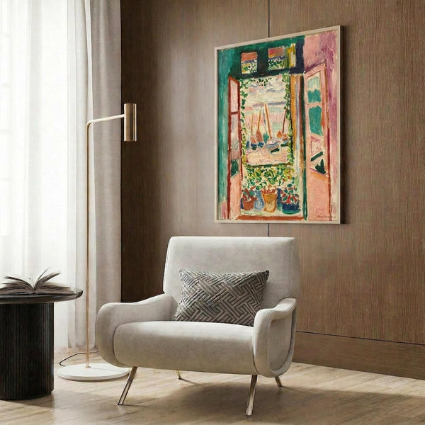 May include: Colorful Matisse-style painting hanging on wood-paneled wall above cream upholstered armchair with geometric pillow. Artwork shows vibrant green, pink, and orange interior scene with open window view. Modern reading nook with brass floor lamp and dark side table with open book.