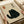 Hands holding a beige textured art print featuring a black cat illustration with yellow eyes in Japanese ink wash style. The print includes Japanese calligraphy characters and a red seal stamp in the upper portion. The artwork is displayed on white paper wrapping with a beige ribbon visible in the background.