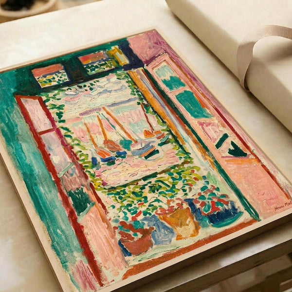 Colorful Fauve-style painting showing an interior view through open windows overlooking a harbor with sailboats. Bold brushstrokes in vibrant greens, pinks, oranges and blues create window frames, potted plants on the windowsill, and a scenic water view beyond. The artwork is displayed in an open art book with cream-colored pages, photographed on a white surface next to rolled white paper.