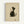Framed artwork showing a minimalist black and white cat sitting in profile, head tilted upward. The cat has dark fur on its back and head with white chest and face, rendered in simple brushstrokes on cream textured paper. A small red stamp seal appears in the bottom right corner. The piece is displayed in a thin natural wood frame against a white wall.