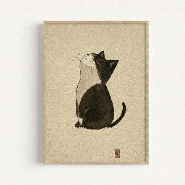 Framed artwork showing a minimalist black and white cat sitting in profile, head tilted upward. The cat has dark fur on its back and head with white chest and face, rendered in simple brushstrokes on cream textured paper. A small red stamp seal appears in the bottom right corner. The piece is displayed in a thin natural wood frame against a white wall.