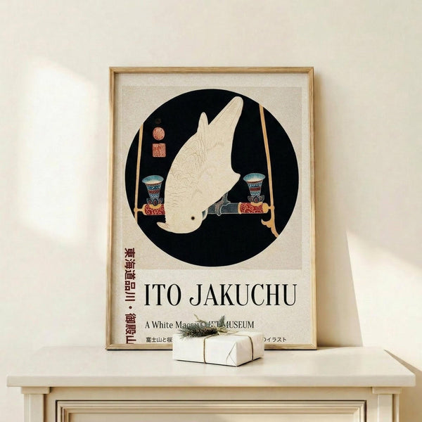 May include: Framed poster featuring a white macaw in profile within a black circle, displayed on a light wood console table. The artwork shows Japanese-style illustration with decorative vessels and red seal stamps. Text reads "ITO JAKUCHU" and "A White Macaw MUSEUM" below the circular design. Small wrapped gift box with greenery sits beside the wooden frame against a cream wall.