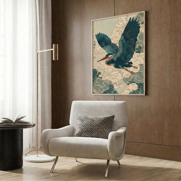 May include: Japanese-style artwork depicting a blue-green heron with outstretched wings soaring through swirling clouds, displayed in a light wooden frame on wood-paneled wall. Modern reading nook setting with cream upholstered armchair, geometric patterned pillow, brass floor lamp, and round side table with open book. Warm natural lighting from window with sheer curtains creates cozy atmosphere.