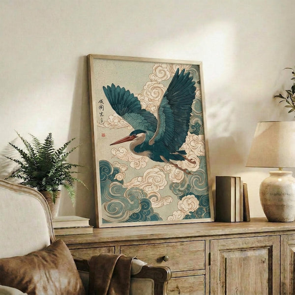 May include: Framed Japanese-style artwork featuring a blue-green heron with outstretched wings soaring through swirling clouds and traditional wave patterns, displayed on a rustic wooden sideboard alongside potted ferns, ceramic vases, and books in a neutral-toned living room with beige walls and leather furniture