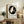 May include: Framed poster featuring a white parrot silhouette in black circle with decorative elements and "ITO JAKUCHU" text below, displayed on rustic wooden sideboard next to fern plant, books, ceramic vase, and beige upholstered chair in neutral-toned living room setting with natural lighting.