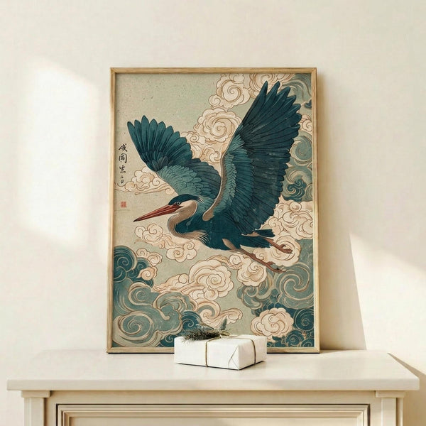 May include: Framed Japanese-style artwork featuring a blue-green heron with outstretched wings flying through swirling clouds and mist, displayed on a light wood console table next to a small white wrapped gift with greenery, against a cream-colored wall with natural lighting casting soft shadows.