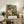 May include: Framed botanical poster featuring a vibrant hummingbird with spread wings hovering near a large pink peony flower, surrounded by lush green foliage in William Morris textile style. The print sits on a rustic wooden sideboard next to books, a ceramic vase, and fern plant in a bright living room setting with cream walls and beige furniture.