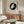 May include: Japanese art poster featuring white macaw in black circle on beige background, displayed in wooden frame above walnut credenza. Modern living room with cream upholstered chair, glass-top coffee table, brass floor lamp. Clean minimalist styling with natural wood tones and neutral colors throughout the space.