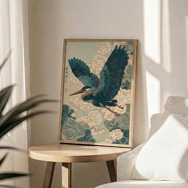 May include: Japanese-style artwork featuring a blue-green heron with outstretched wings flying through stylized swirling clouds in teal and cream colors, displayed in a thin wooden frame on a round wooden side table next to a beige upholstered chair, with natural sunlight casting shadows across white walls and a plant visible in the corner.