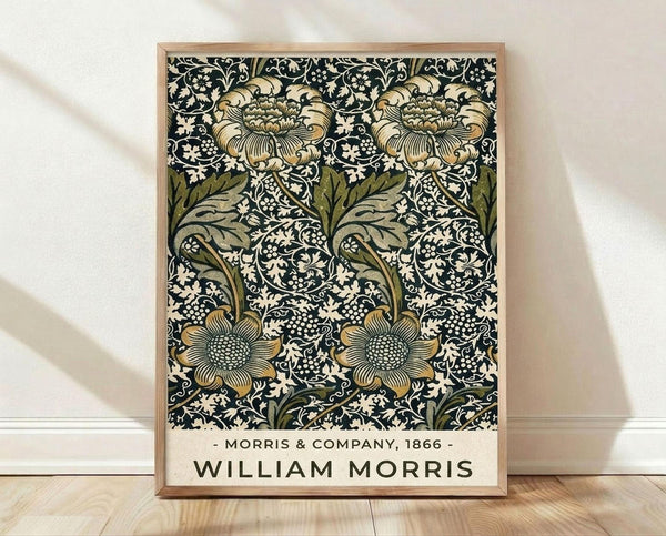 May include: Framed poster print with William Morris floral pattern in dark navy, cream, olive green and gold tones, featuring ornate blooming flowers and decorative leaves in Victorian Arts and Crafts style, displayed in light wood frame leaning against white wall on wooden floor with soft natural lighting