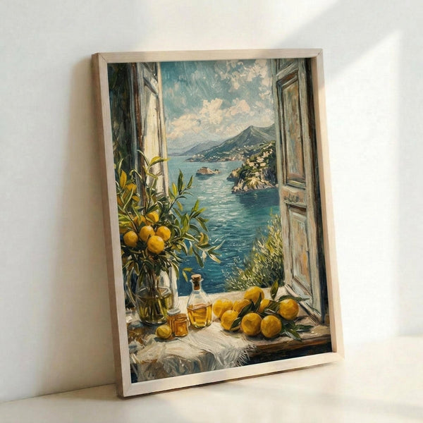 Framed poster print leaning against white wall showing Mediterranean coastal scene viewed through open wooden window shutters. Foreground features windowsill with yellow lemons, citrus branch in glass vase, and amber bottles. Turquoise blue water stretches toward distant mountains and hillside villages under cloudy sky. Warm painting style with rich blues, yellows, and earth tones in light wood frame.
