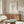 May include: Botanical poster with blue illustration of dried flowers in a glass vase displayed above a mid-century modern walnut credenza in a neutral living room. The framed artwork features vintage-style line drawing against cream background, positioned between a white sculptural chair and brass table lamp, with an oval glass coffee table in foreground.