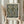 May include: Hands holding a framed botanical print featuring William Morris's ornate floral pattern in navy blue, sage green, and cream tones. The vintage-style design shows detailed flowers, leaves, and decorative scrollwork. Light wood frame against neutral curtain backdrop with dried pampas grass visible on left side.