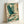 May include: A framed print leaning against a white wall showing a blue heron in flight with outstretched wings soaring through stylized clouds and waves. The artwork features teal, turquoise and cream colors in traditional Japanese woodblock print style with decorative swirling cloud patterns and wave motifs. The print is displayed in a light wood frame and includes red Japanese characters in the upper right corner.